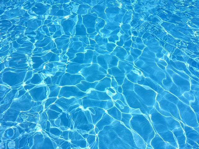 プールサイドに立つ水着姿の女性が笑顔で水泳帽とゴーグルを持っている様子